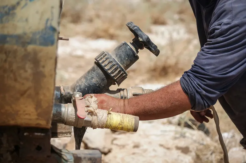 Hands closing a valve on a pipe outdoors