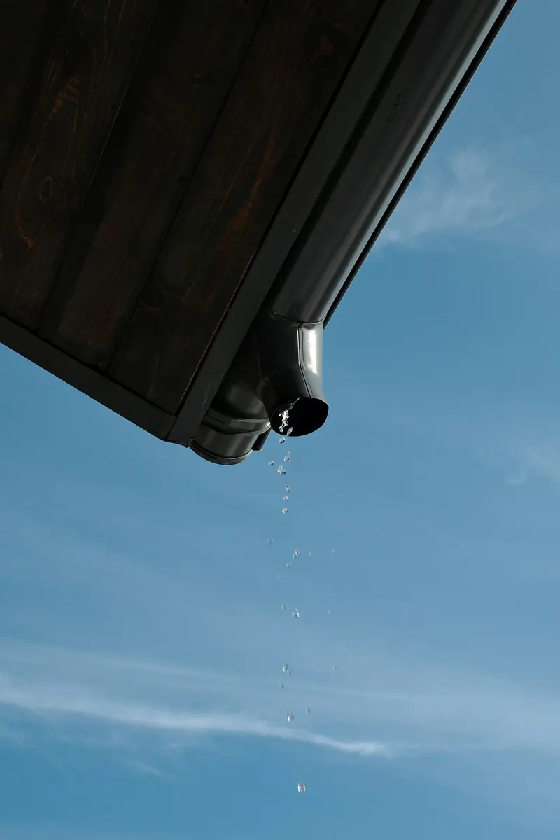Downspout dripping water against a blue sky