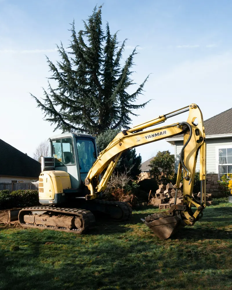 Yellow excavator parked on a lawn beside houses