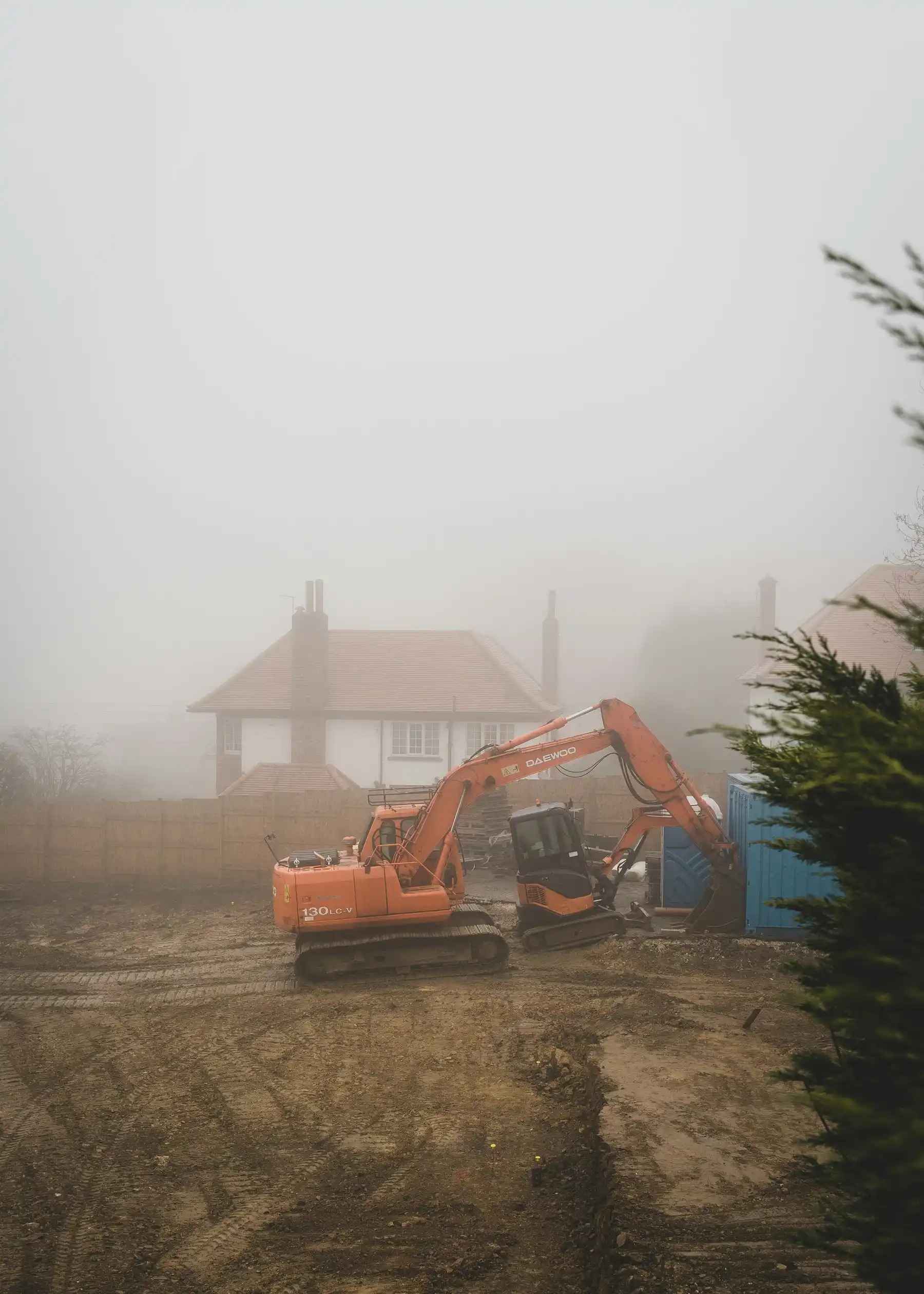 Excavator working beside a house in morning fog