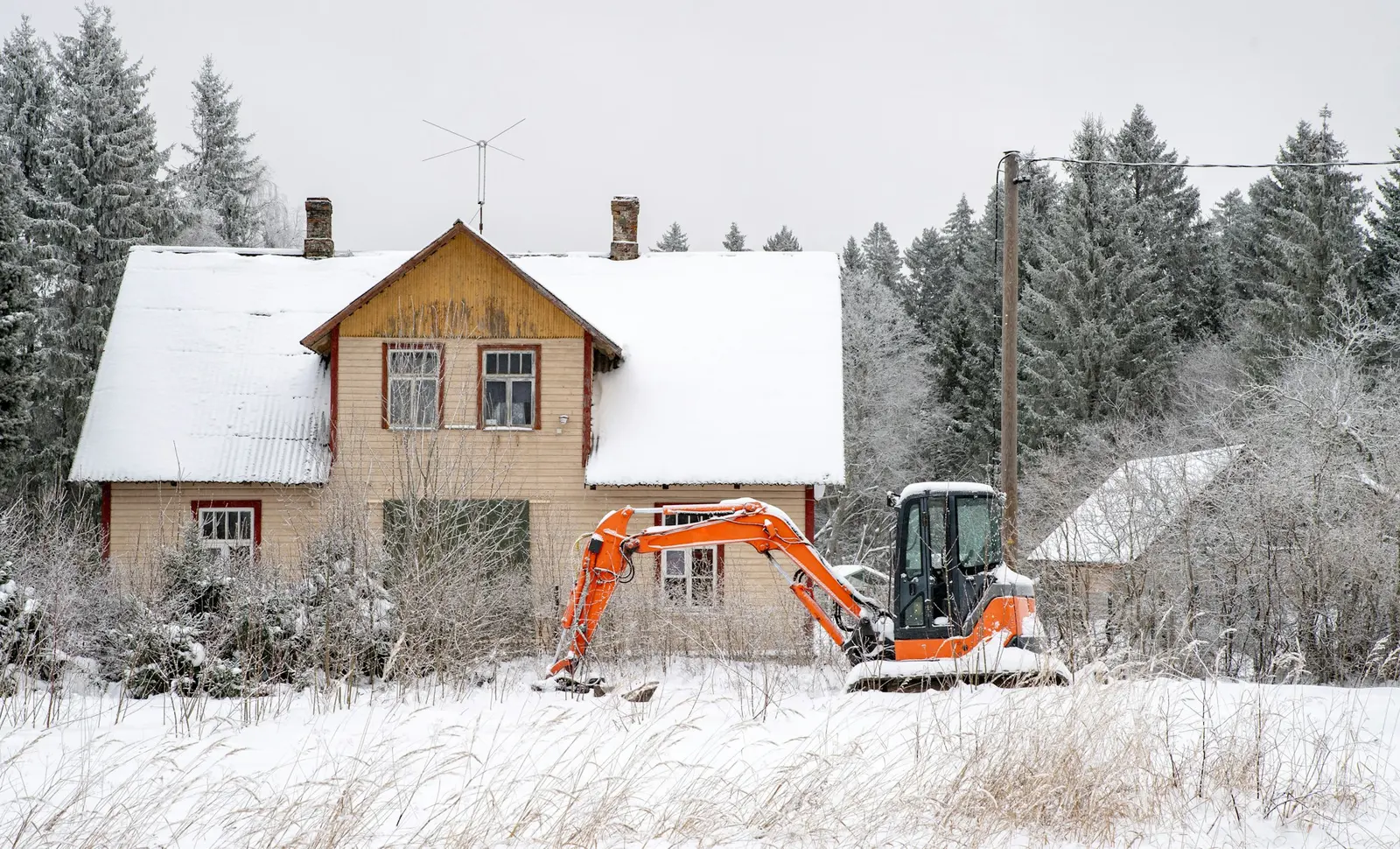 Orange mini excavator working beside a house in fresh snow
