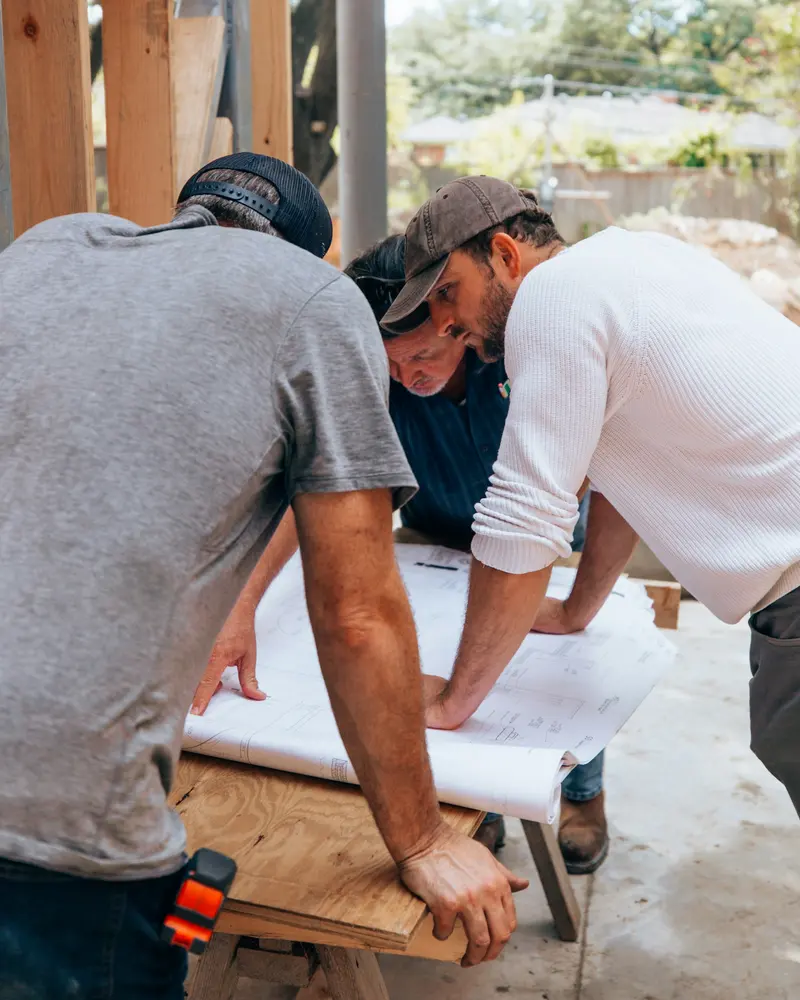 Three people reviewing drawings spread on a table
