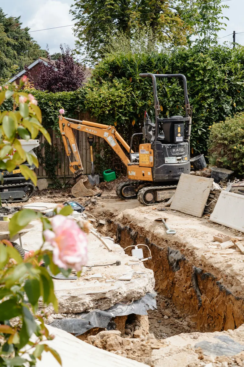 Narrow trench opened along a garden wall by a mini excavator