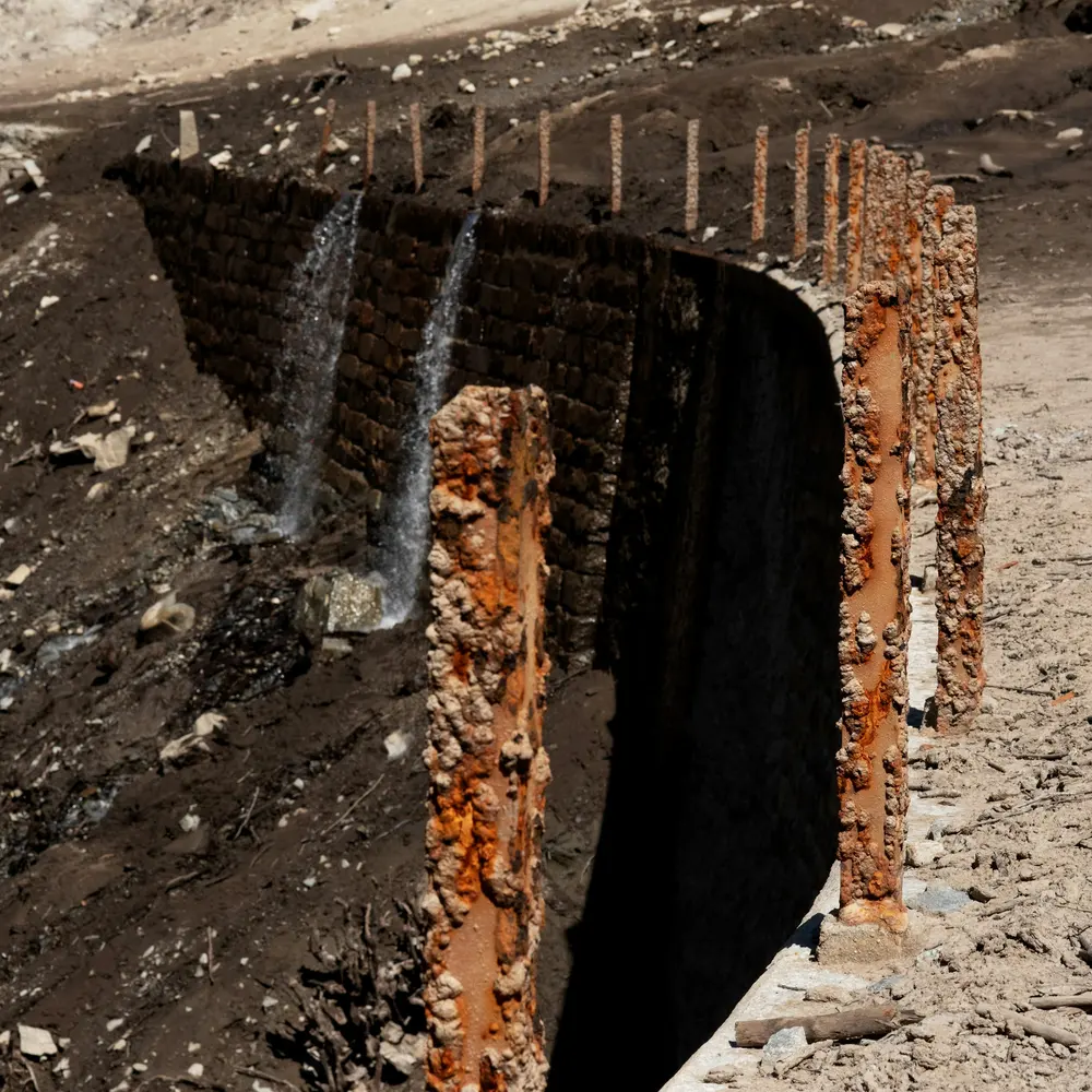 Water pouring through an opening in a rusted retaining wall